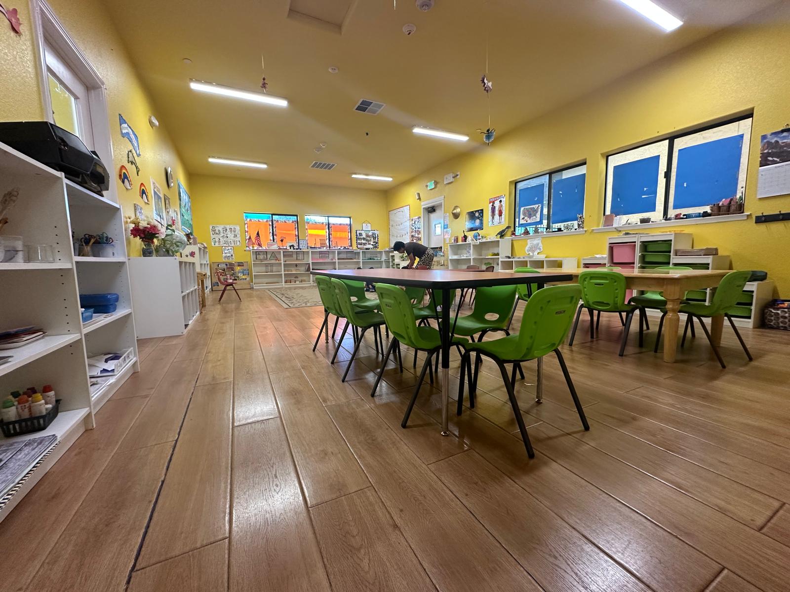 Colorful classroom with yellow walls, green furniture, and creative artwork displays, designed for children's learning and activities.