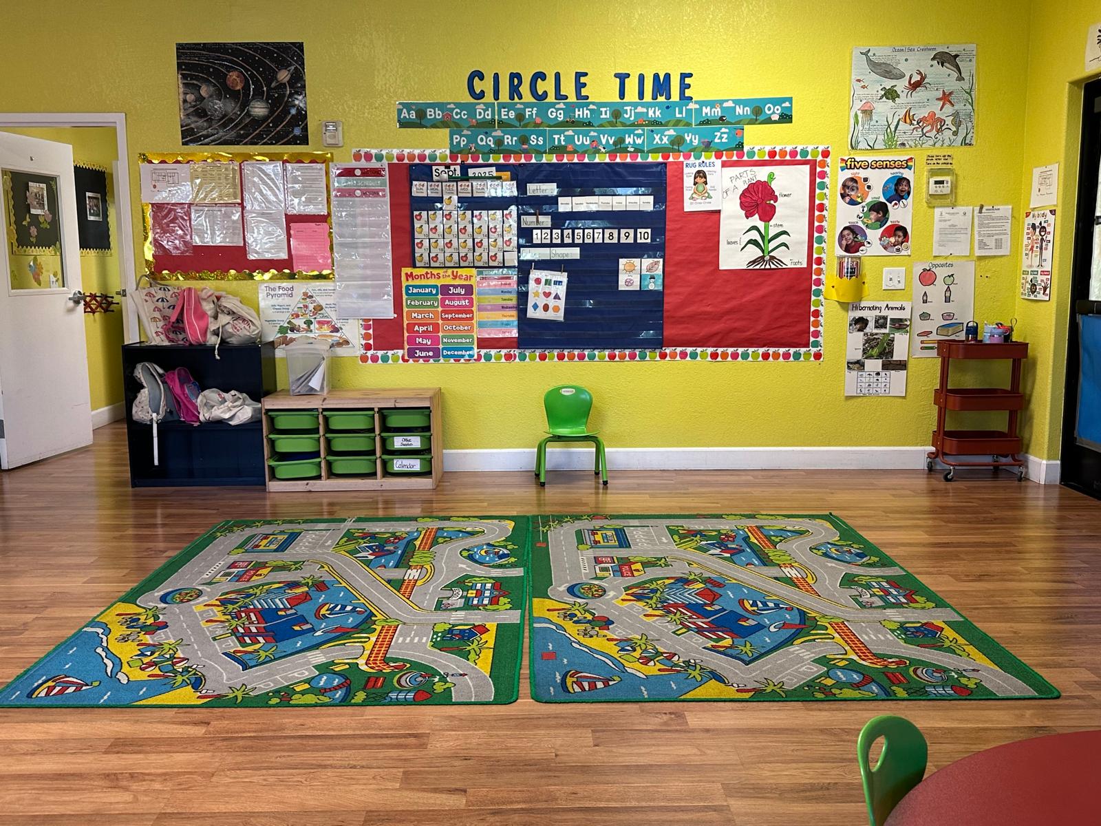 Bright classroom featuring colorful educational posters, a "Circle Time" area, and patterned rugs depicting roads and buildings, fostering interactive play.