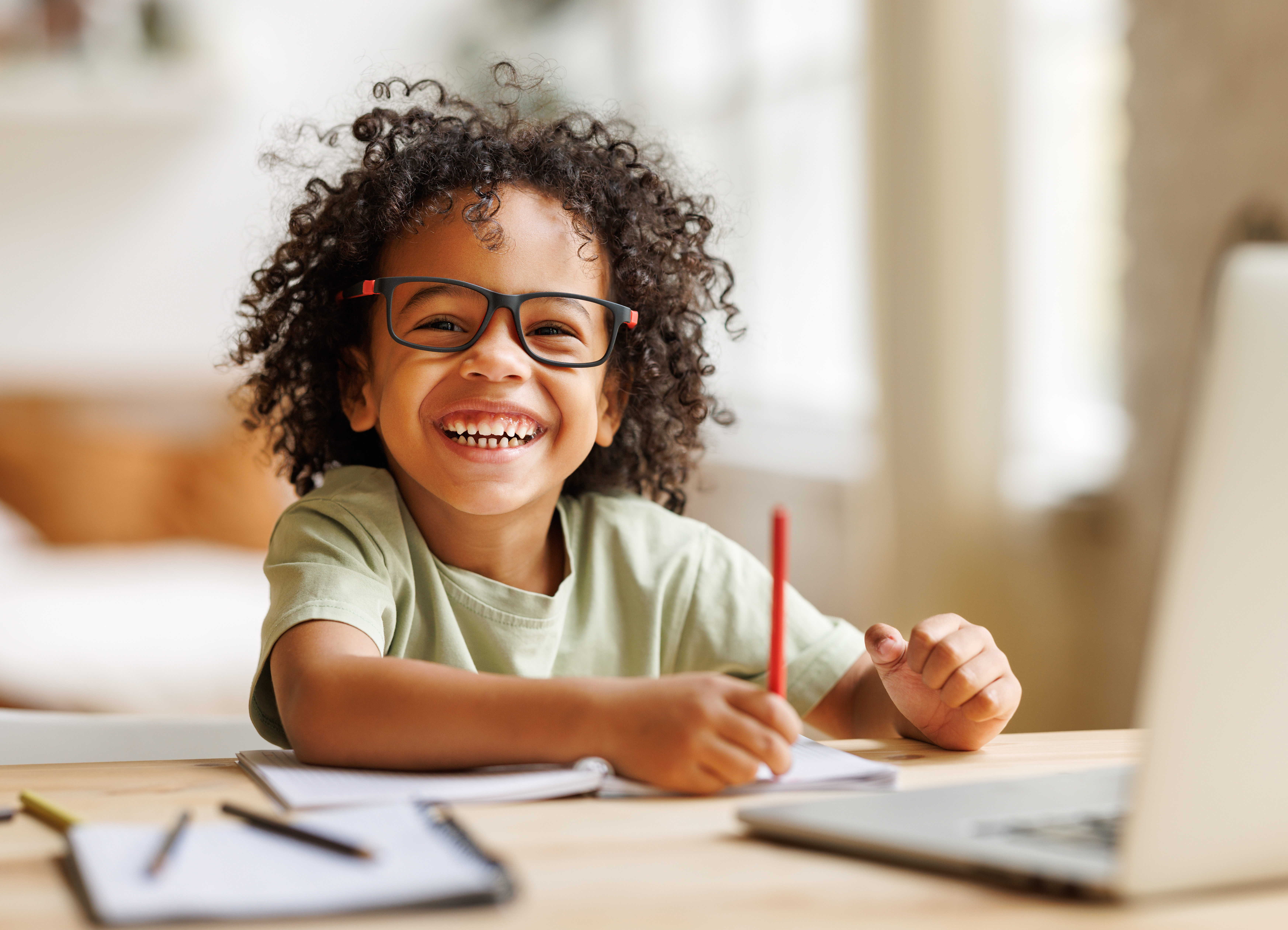 Distance education. Smiling african american child schoolboy studying online on laptop at home, sitting at table and communicating with teacher through video call on computer; Shutterstock ID 2120879519; purchase_order: Pro Serv; job: ; client: ; other: