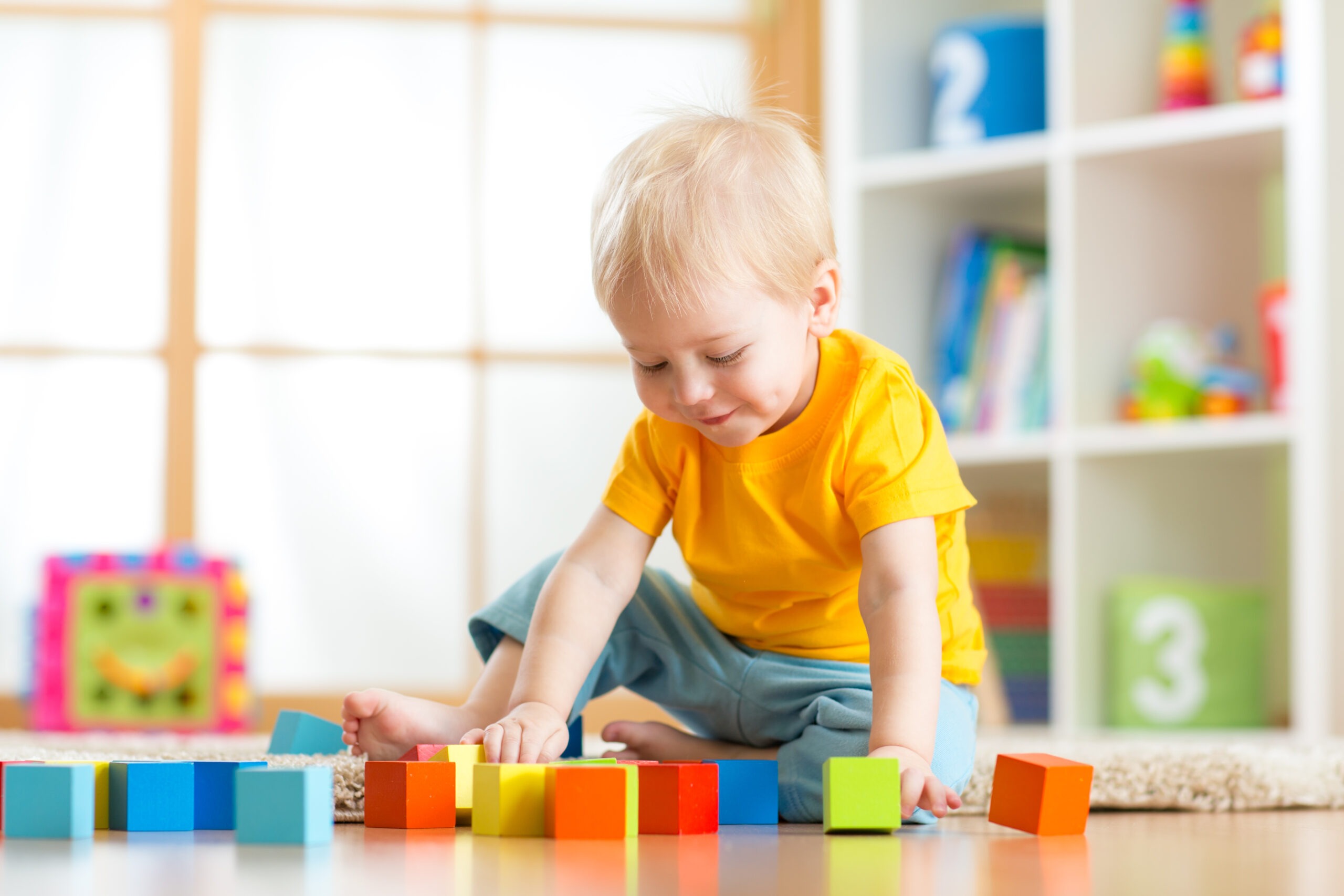 Preschooler child playing with colorful toy blocks. Kid playing with educational wooden toys at kindergarten or day care center. Toddler in nursery room.
